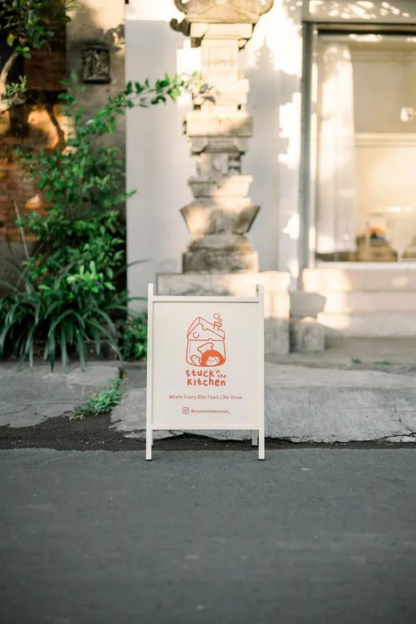 The cream SINK A-frame sign on the street outside, by a Balinese stone gate